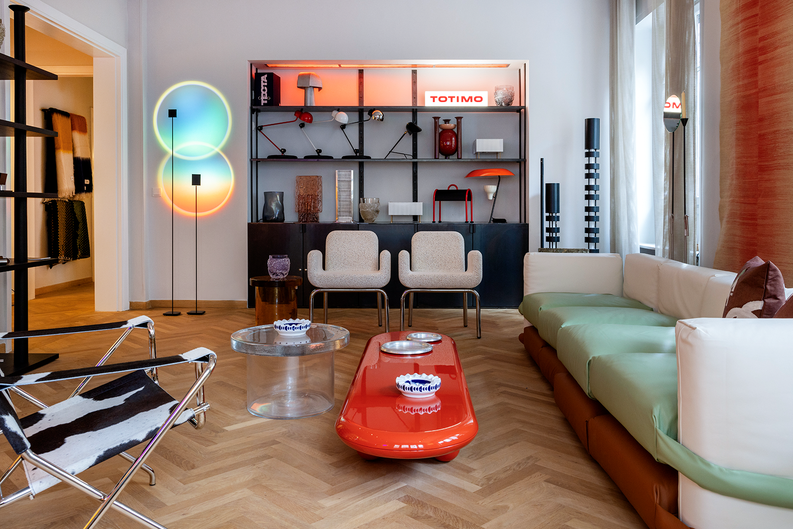 Modern living room with a red coffee table, white chairs, and a large circular light fixture.